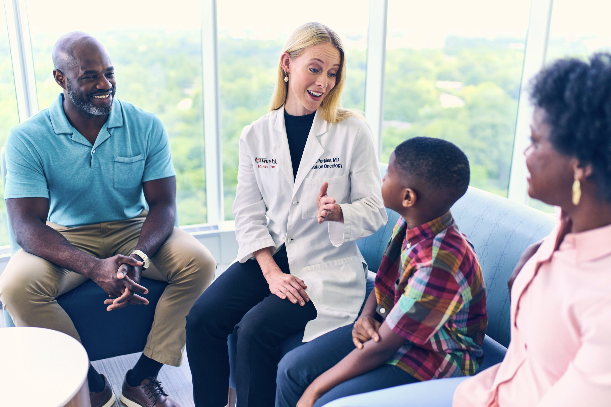 Female doctor happily conversing with a family: adult male, a male child, and an adult female