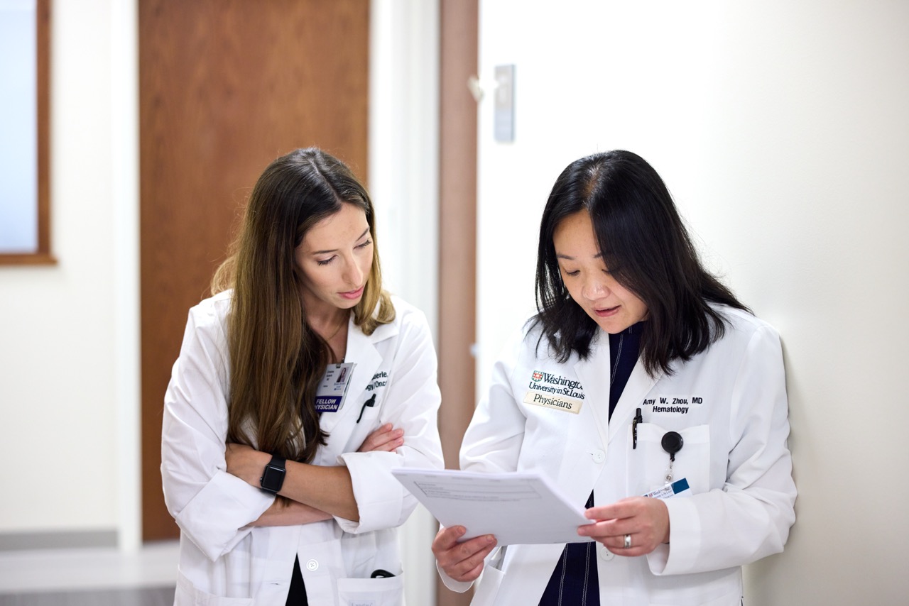 Two physicians converse while reviewing a patient file