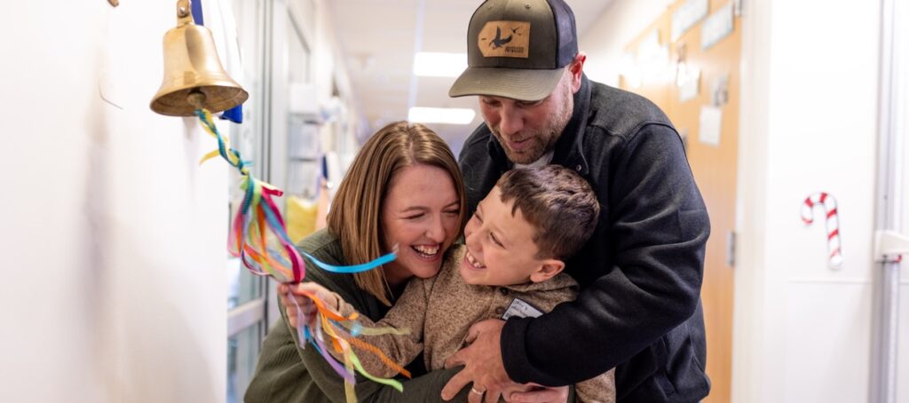 boy ringing bell with parents hugging