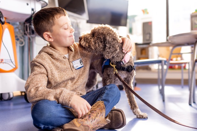 a kid sitting crossed leg looks lovingly at a dog