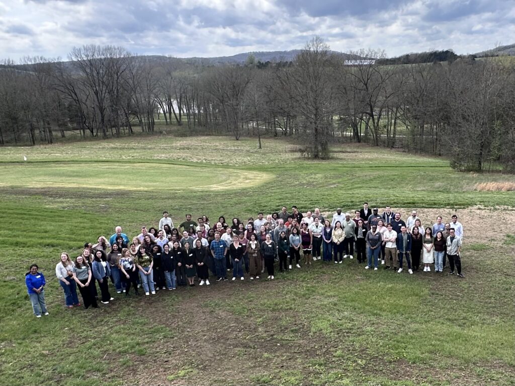 A large group of people posing together in an outdoor grassy field.