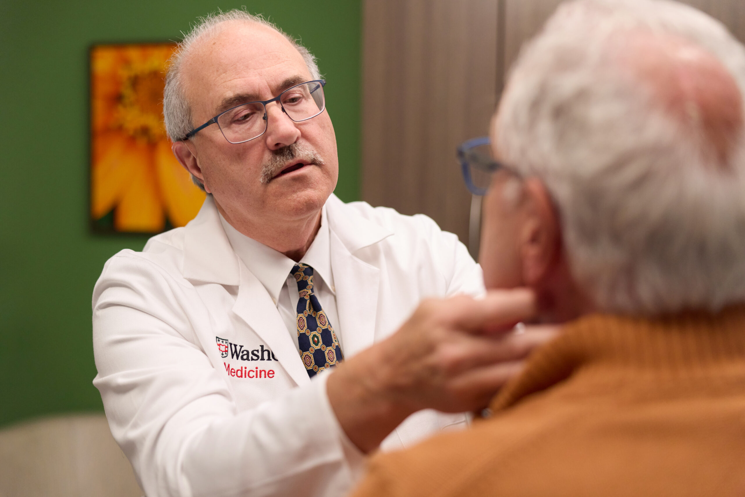 Dr. Doug Adkins, MD, wearing a WashU Medicine lab coat, performs a physical neck examination on a patient.