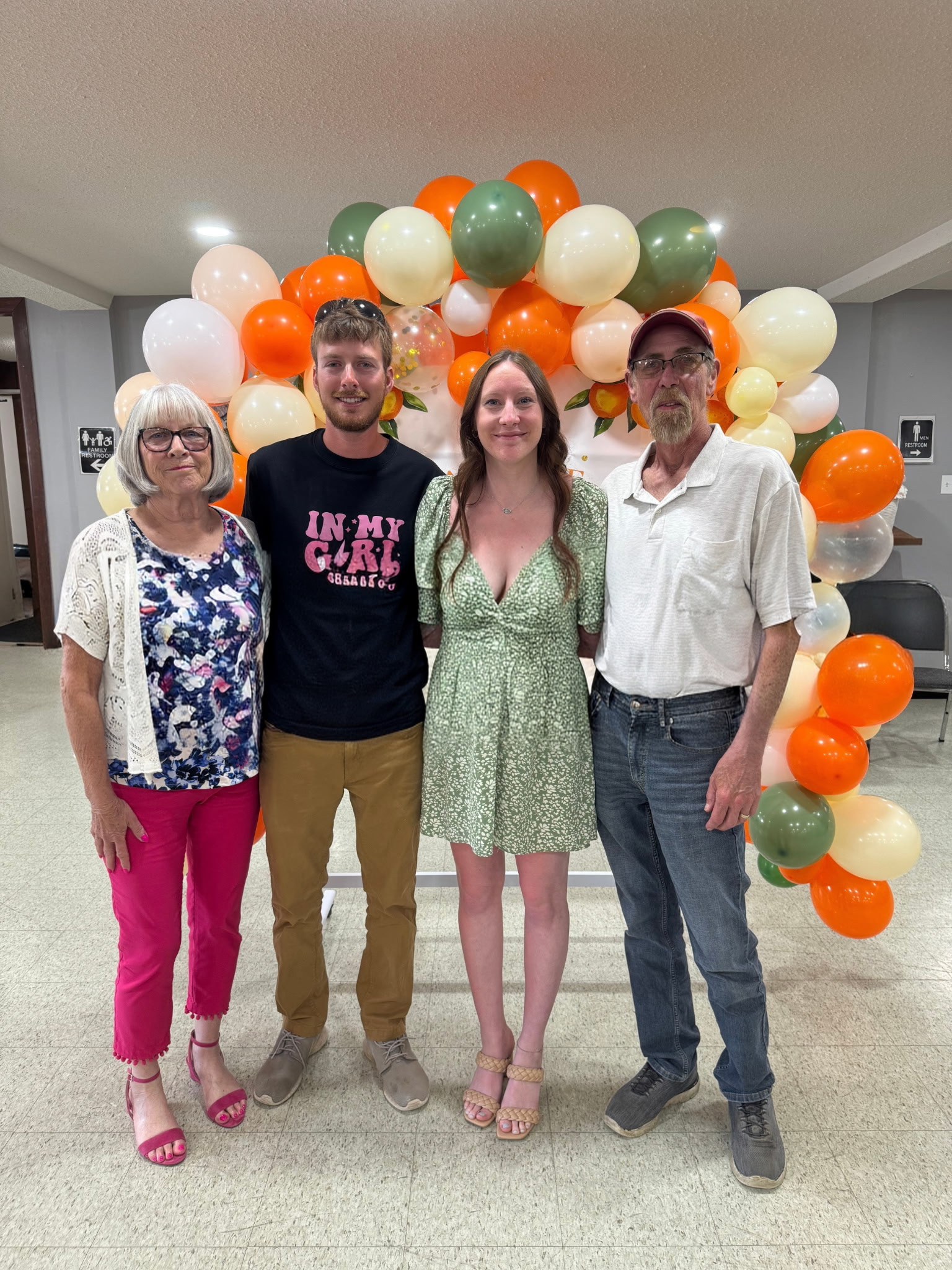 Two parents stand next to adult children in front of an orange and white balloon arch