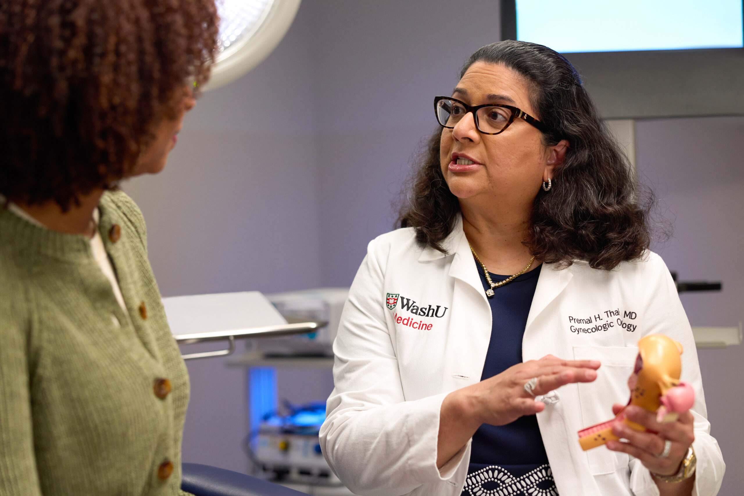 Dr. Premal Thaker, MD, MS, wearing a WashU Medicine lab coat, holds an anatomical model while speaking to a patient.