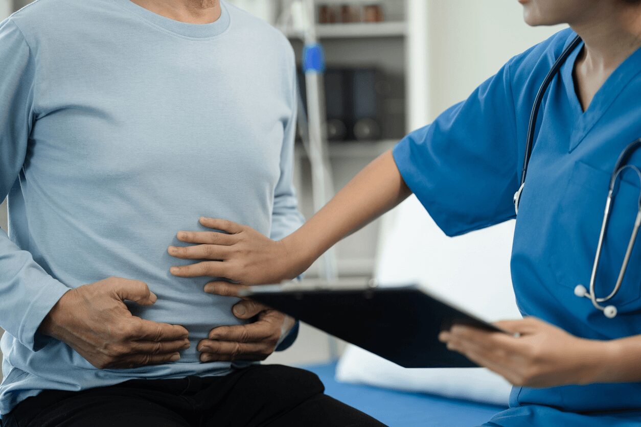 Healthcare provider in blue scrubs examining a patient's abdomen while holding a clipboard