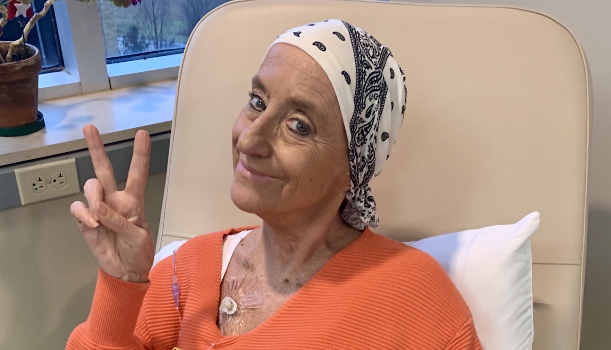 Woman in orange sweater with head scarf shows peace fingers