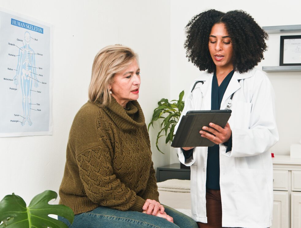 A physician in a white coat speaks with an older patient in a clinic
